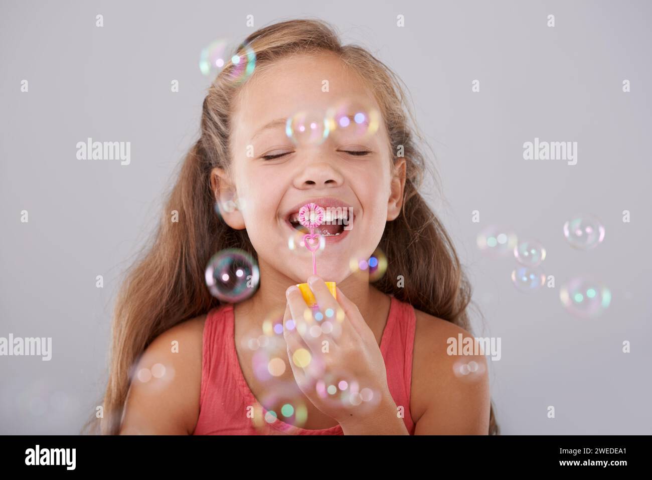Glückliches, kleines Mädchen und Blasen im Studio von Spielzeug, süße und lustige Spiele für die Hand Augen Koordination. Kind, Augen geschlossen und mit dem Blasstab spielen Stockfoto