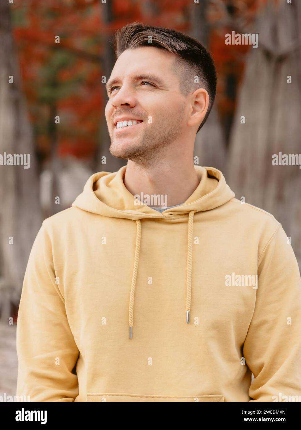 Schöner Mann im herbstlichen Wald. Porträt eines lächelnden kaukasiers in gelben Hoodies Stockfoto