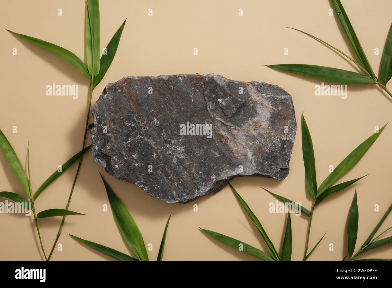Grauer Stein und grüne Bambusblätter sind auf braunem Hintergrund verziert. Minimale Szene mit leerem Platz für die Anzeige von kosmetischen Produkten. Draufsicht, flach. Stockfoto