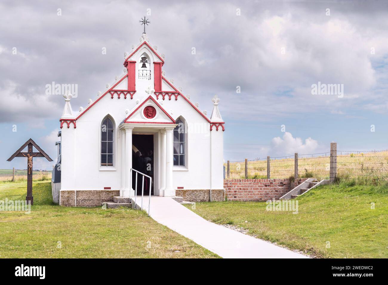 Kleine kunstvoll verzierte katholische Kapelle Touristenattraktion auf den Orkney-Inseln in Schottland mit einem gemähten Rasen davor und einem Kreuz mit Jesus an der Seite Stockfoto