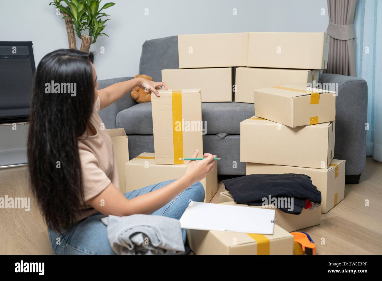 Asiatische Frau, die eine Checkliste macht, während sie für ein neues Zuhause packt. Stockfoto