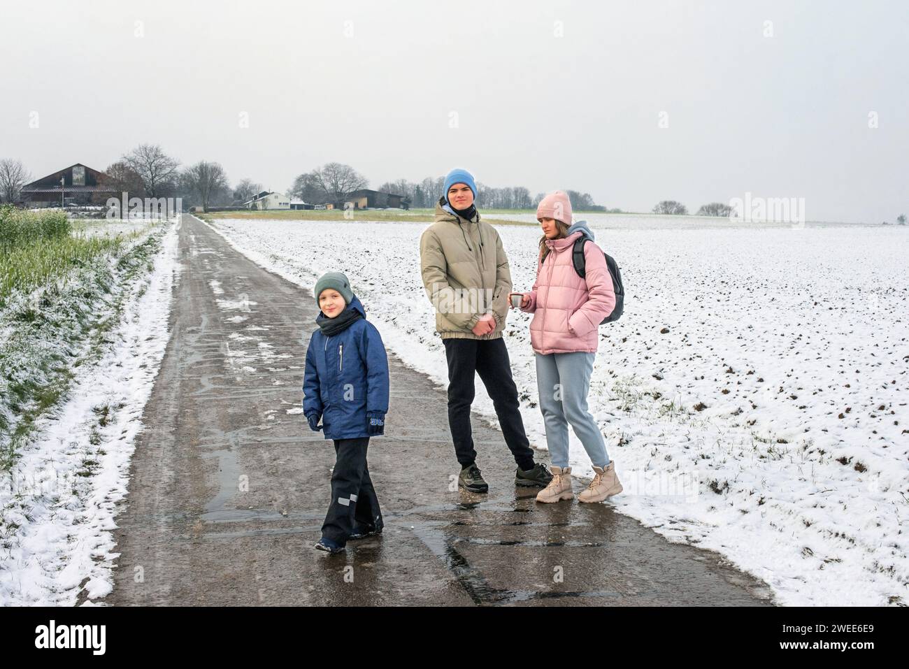 Winter Family Bliss: Mutter und zwei Söhne genießen einen Spaziergang durch die schneebedeckte Landschaft. Winter, Schnee, Mutter, zwei Söhne, Familie, ländliche Straße, schneebedecktes Feld Stockfoto