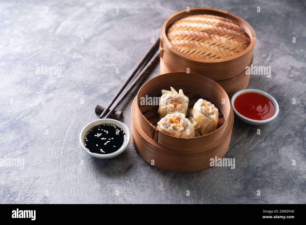 Chinesische gedämpfte Teigtaschen oder Dim Sum in Bambusdampfer auf dunklem abstraktem Hintergrund Stockfoto