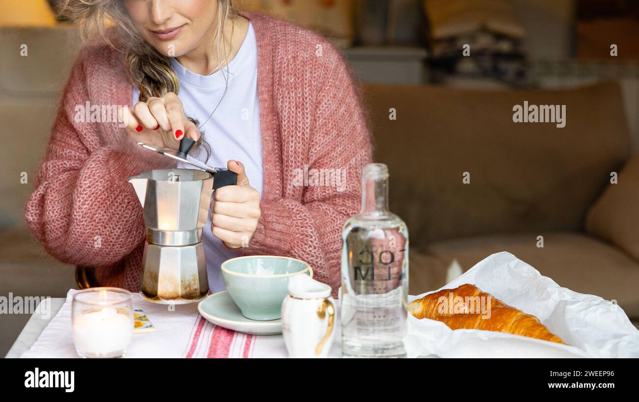 Eine Frau in einem warmen Pullover bereitet Kaffee mit einer Mokakanne zu und genießt ein entspanntes Frühstück zu Hause. Stockfoto