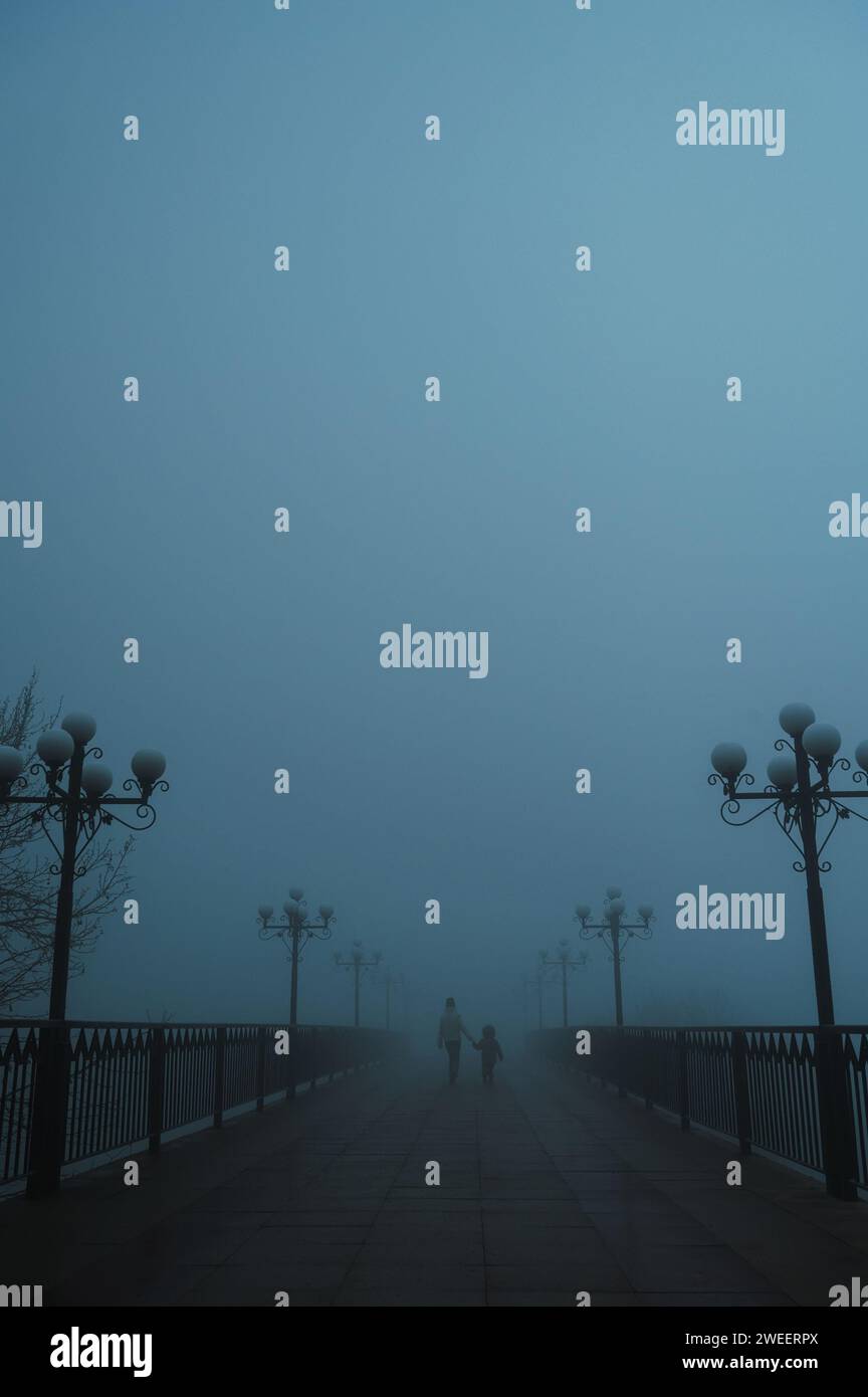 Mystische Silhouetten Rücken einer Frau mit Kind auf einer nebeligen Brücke am Abend im Herbst im Nebelnebel Stockfoto