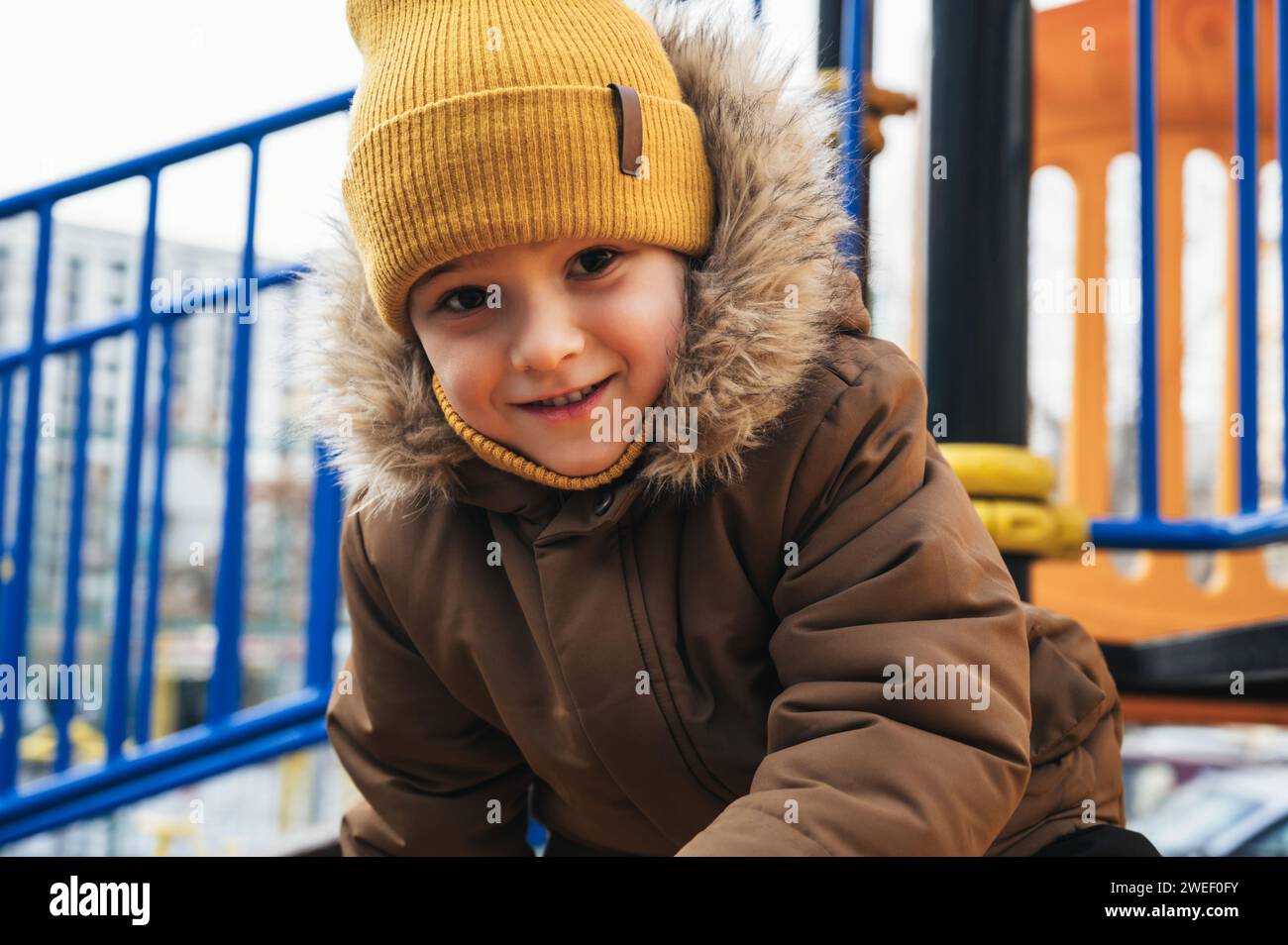 Glückliches Kind, das im Winter im Park auf einer Rutsche auf dem Spielplatz spielt Stockfoto