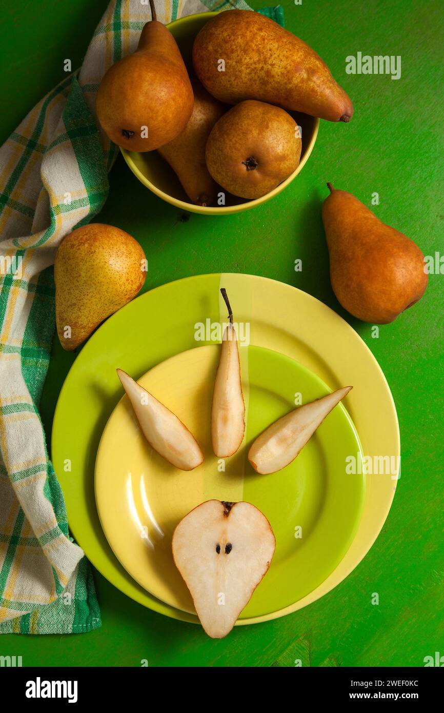 Grüner Teller mit Scheiben und der Hälfte reifer saftiger Birnenfrucht und grünem Küchentuch auf grünem hölzernem Hintergrund. Stockfoto
