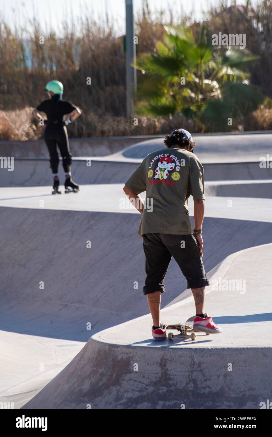 Dynamisches Duo: Rückansicht des Skaters an Bord und des Rollers in der lebendigen Skatepark-Szene Stockfoto