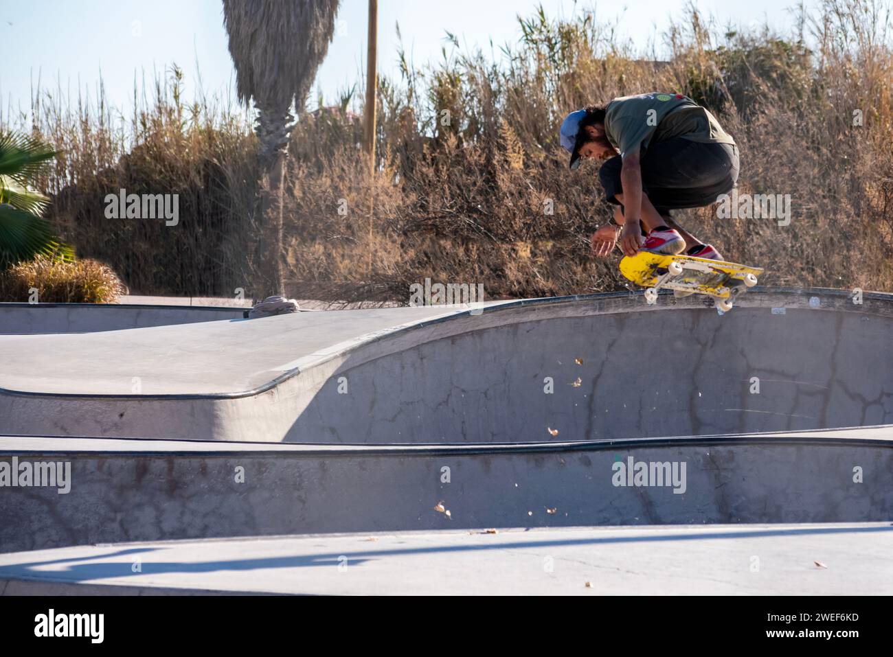 Herbst-Skate-Vibes: Gelber Skateboarder fängt Luft, Blätter wirbeln im dynamischen urbanen Skatepark Stockfoto