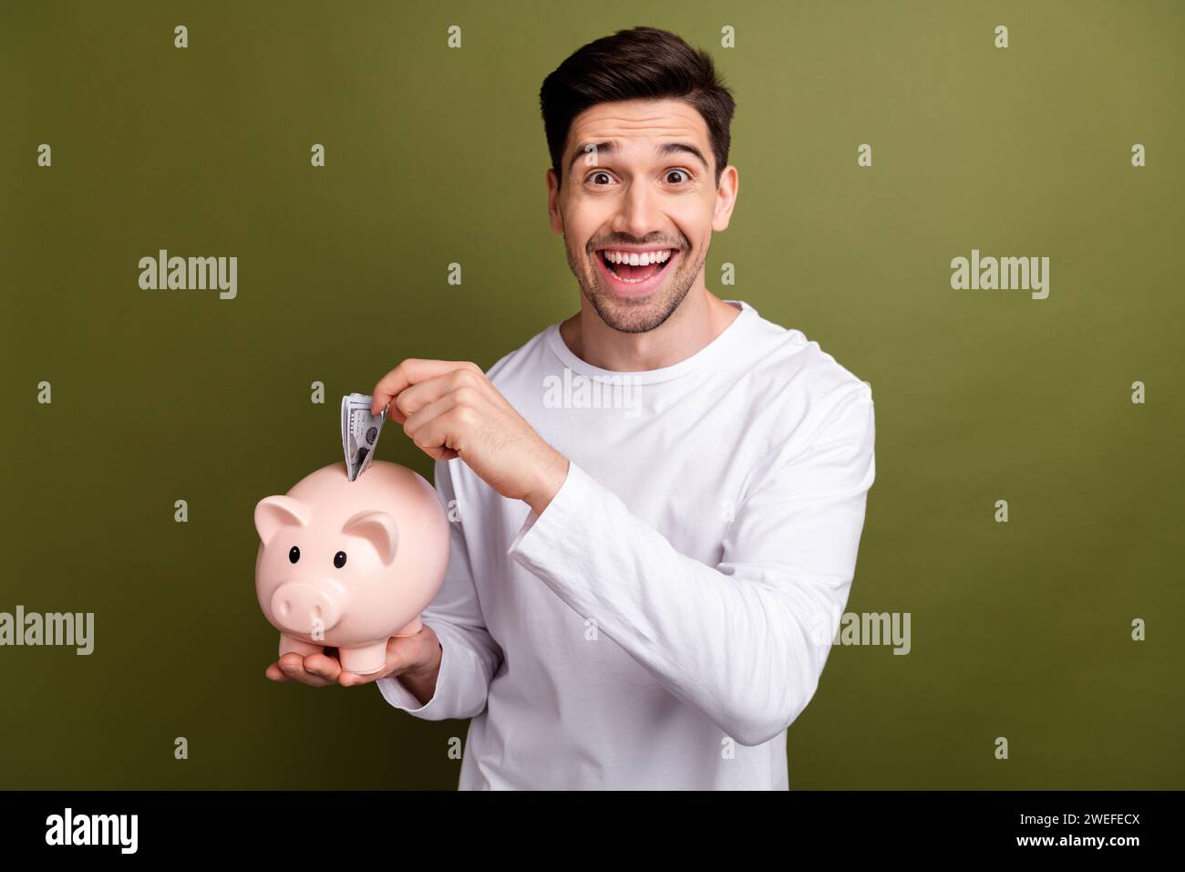 Foto vom Glück, als der junge Mann merkt, dass er den letzten Teil Geld in die Sparkasse gesteckt hat, um Geschäfte zu gründen, isoliert auf khakifarbenem Hintergrund Stockfoto