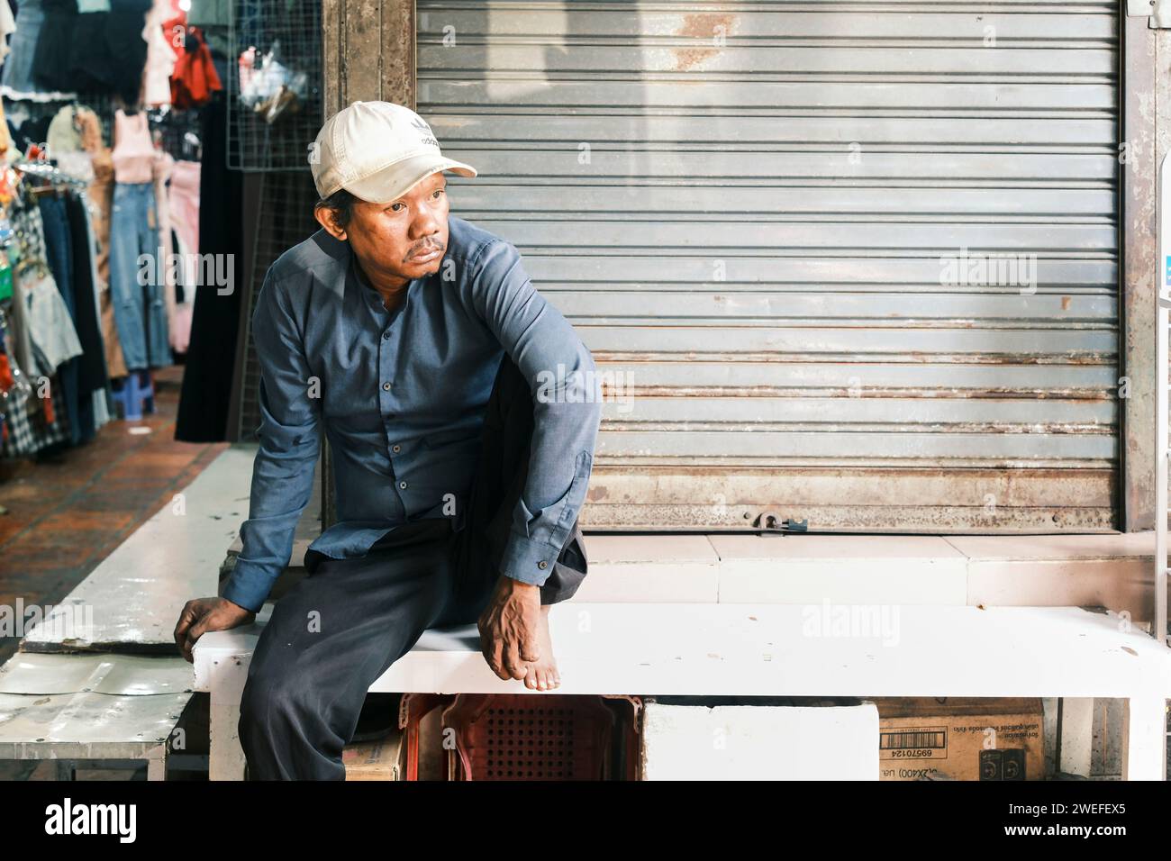 Mann im mittleren Alter, der auf einer Bank sitzt und aus dem BKK Market, Phnom Penh, Kambodscha blickt Stockfoto