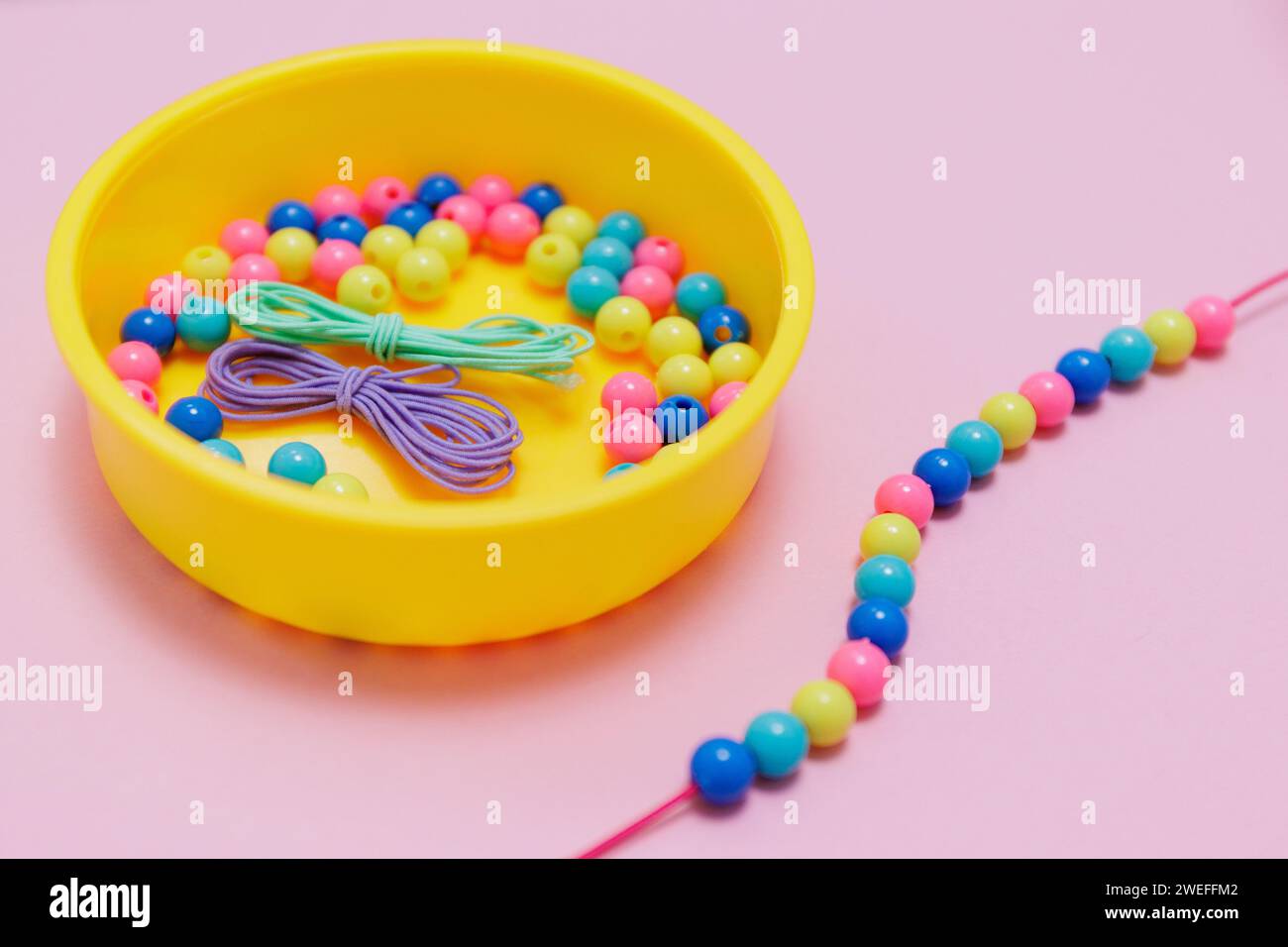 Box mit mehrfarbigen Perlen und handgefertigtem Schmuck auf rosa Hintergrund Stockfoto
