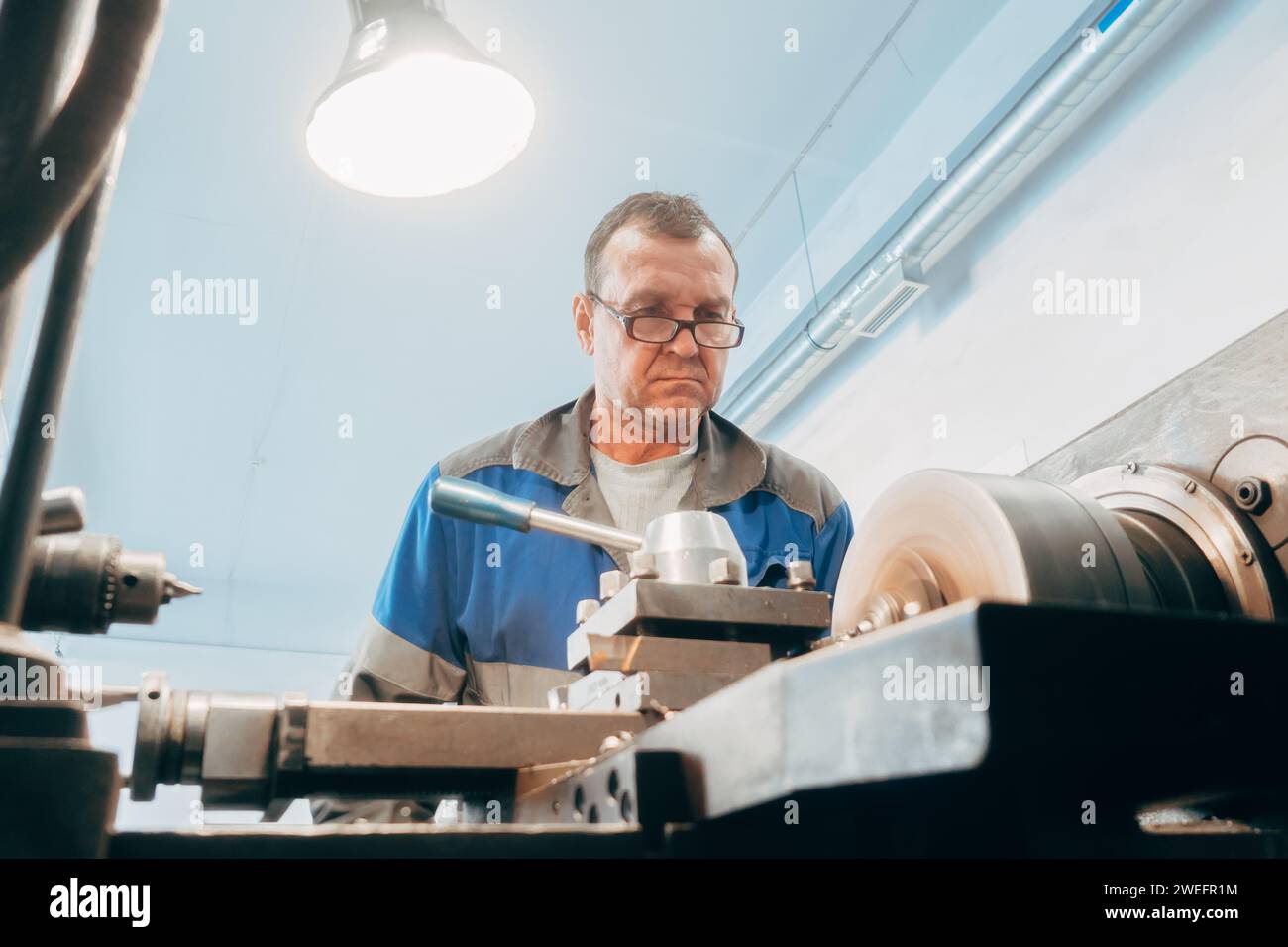 Der ältere turner, 50-55 Jahre alt, arbeitet an der Drehmaschine in der Drehwerkstatt. Vorderansicht. Authentischer Workflow. Stockfoto
