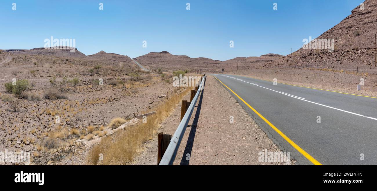Landschaft mit Schichten von Konglomerat und Basalt auf Hügeln und B4 Teerstraße in der Wüste, aufgenommen im hellen Licht des späten Frühlings in der Nähe von Fort Naiams, Namibia, Afri Stockfoto