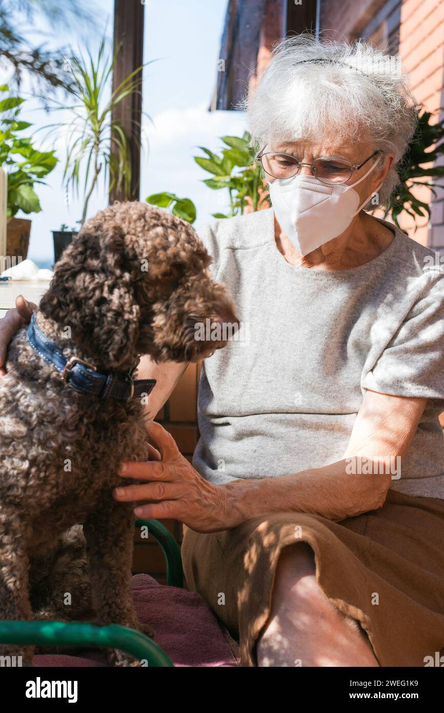 Alte Frau, die eine Gesichtsmaske trägt und ihren Hund hält Stockfoto