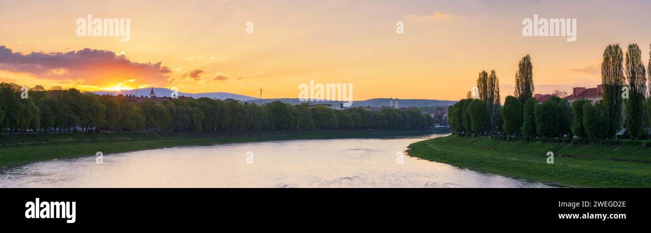 Herrlicher Sonnenaufgang auf dem Fluss uzh der ukraine. Wunderschöne urbane Landschaft der Innenstadt von uschgorod im Frühling. Stadtbild mit grasbewachsenen Böschungen der längsten Stockfoto