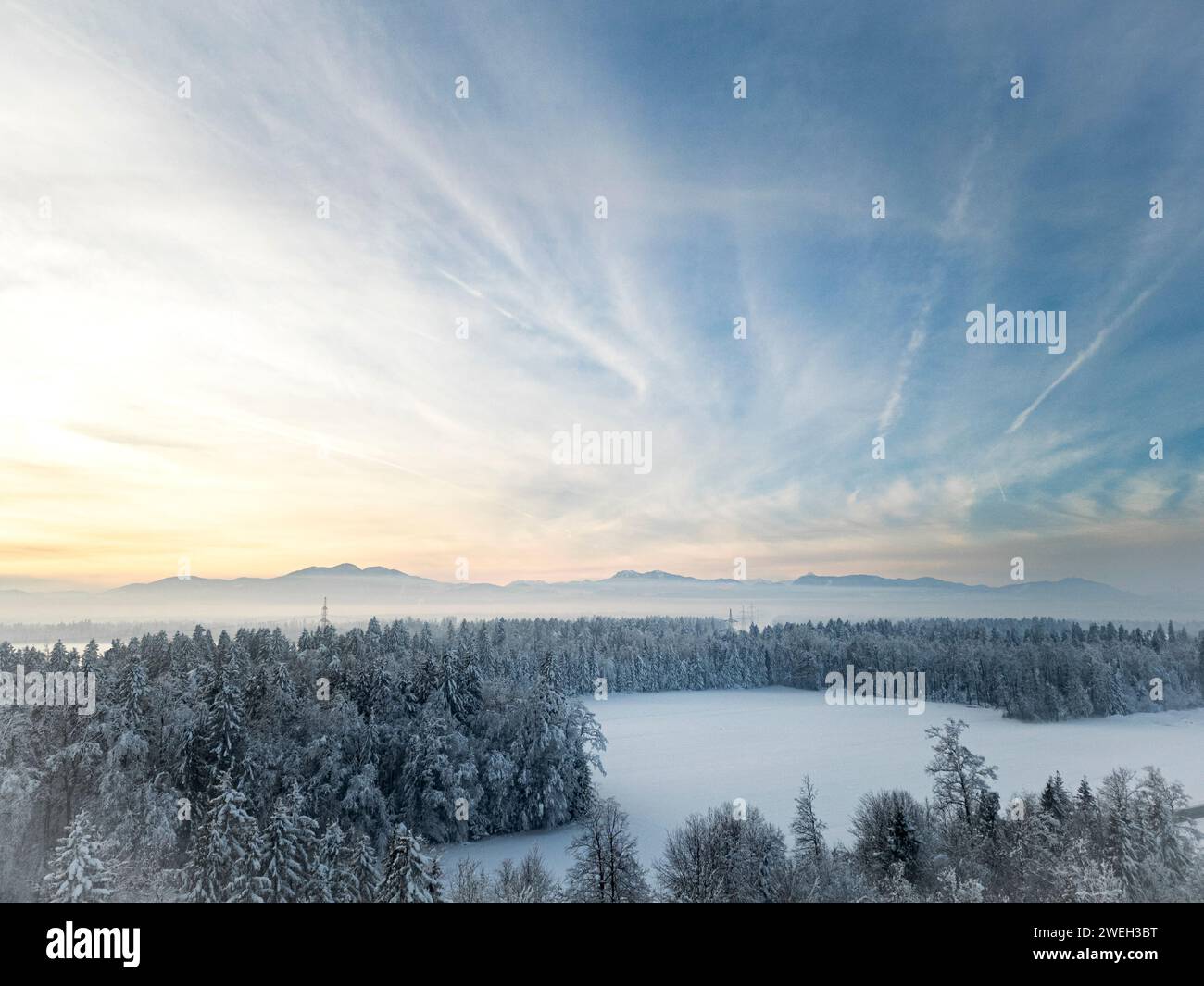 Foto mit einer Drohne von einer wunderschönen, schneebedeckten Winterlandschaft - Wald und eine Lichtung mit Bergen in der Ferne unter dem wunderschönen blauen Himmel mit ge Stockfoto