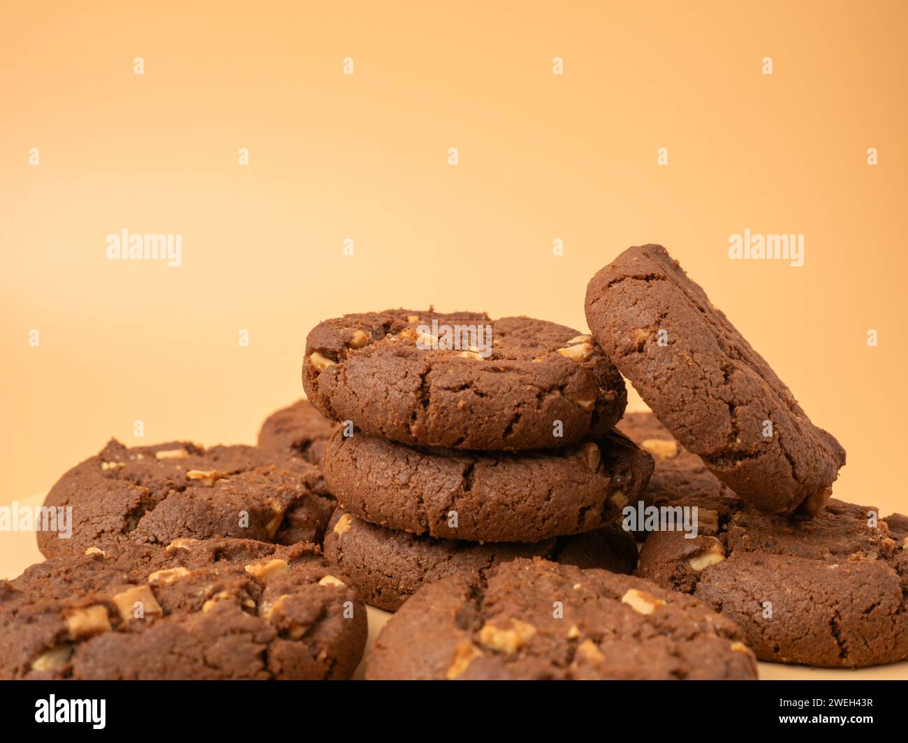 Schokoladige, reichhaltige Kekse mit kontrastierenden weißen Schokoladenchips auf orangem Hintergrund. Kekse mit weißer Schokolade in Nahaufnahme. Stockfoto