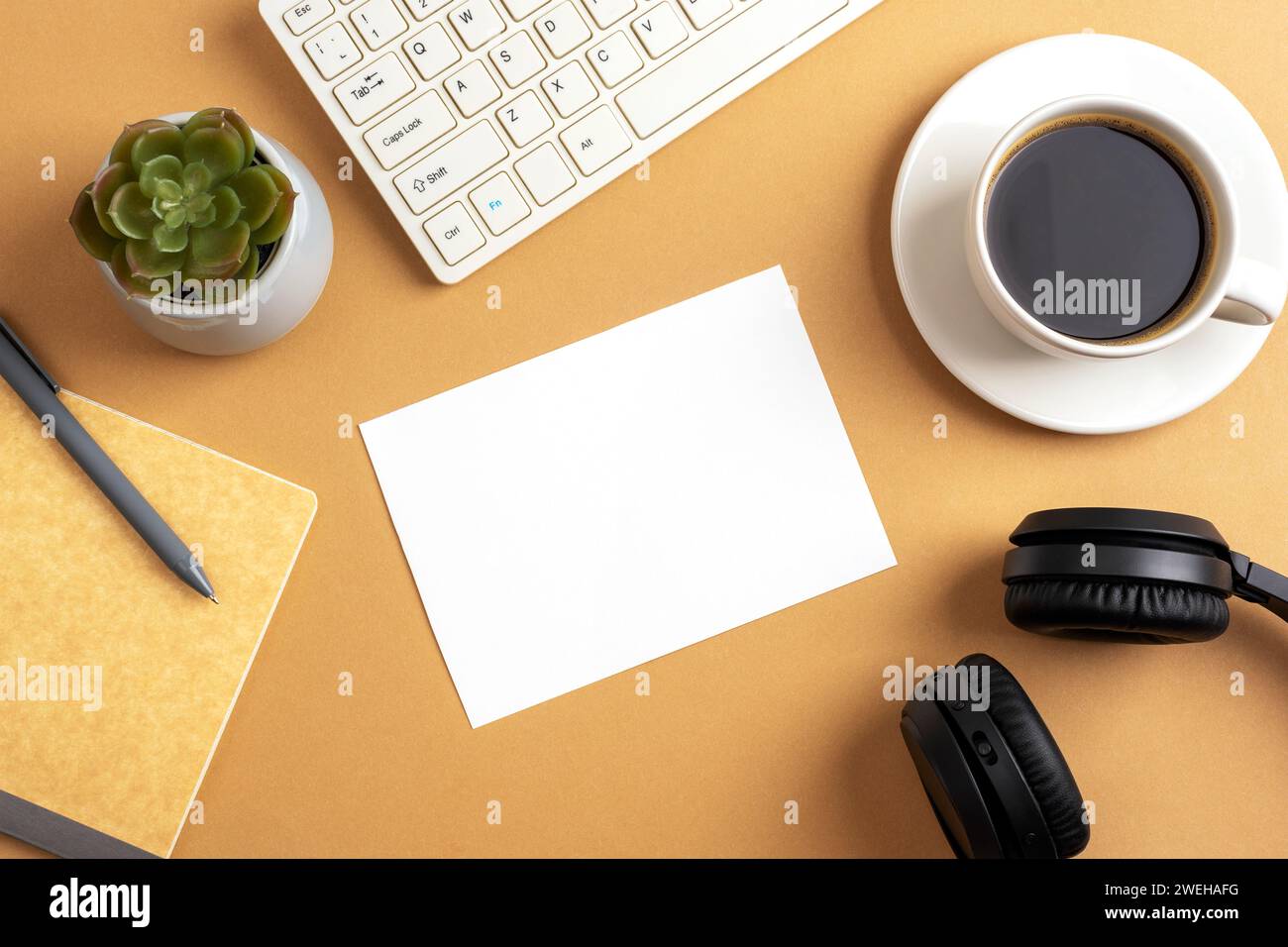 Schreibtisch mit leerer Karte, Kaffeetasse, Notizblock, Tastatur, saftiger Pflanze und Kopfhörern auf braunem Tisch. Draufsicht, flach, Modell. Stockfoto