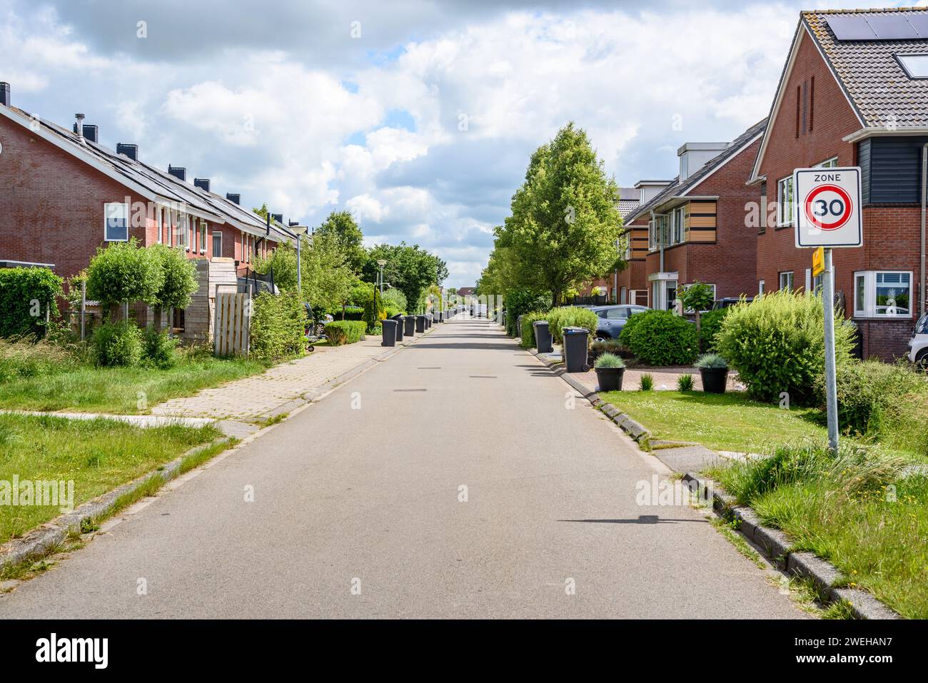 An einem bewölkten Sommertag in einem vorstädtischen Wohnviertel, gesäumt von Einfamilienhäusern aus Ziegelsteinen. Die Mülltonnen sind entlang der Straße. Stockfoto