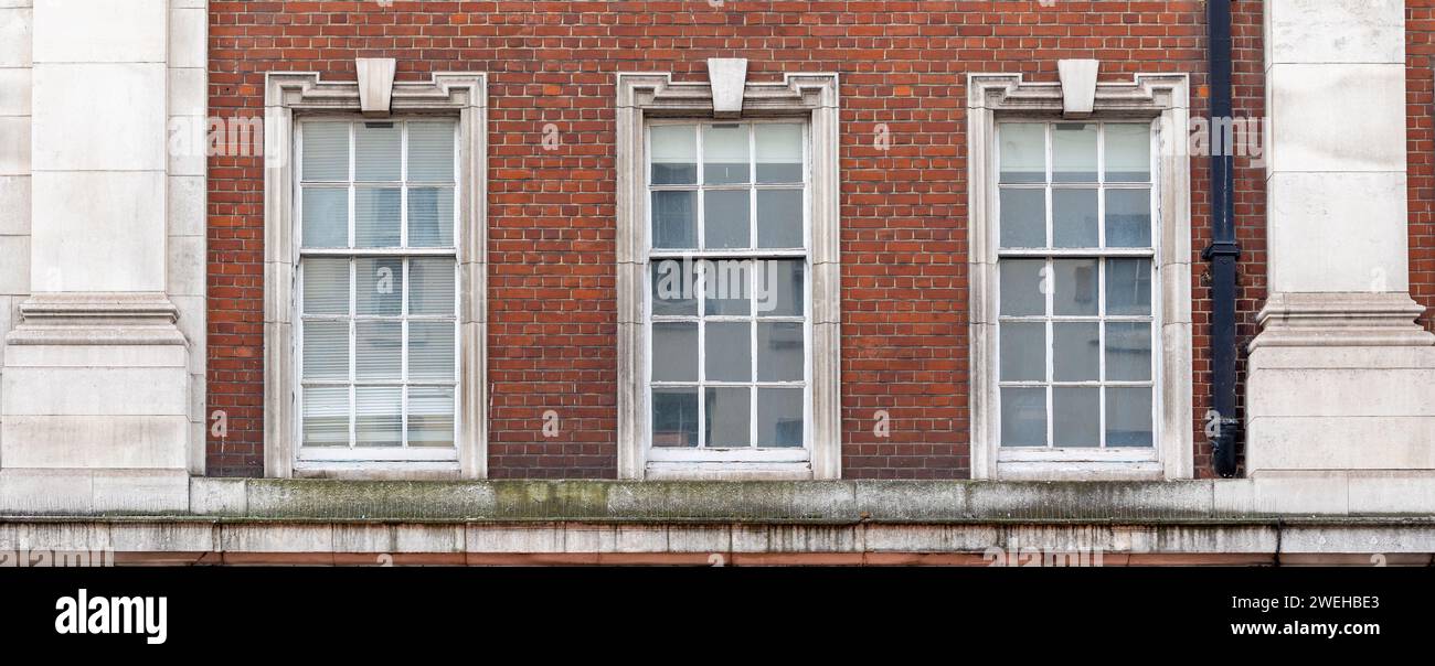Drei ausgerichtete klassische weiße Fenster mit typischer Londoner Architektur mit roter Backsteinmauer Stockfoto