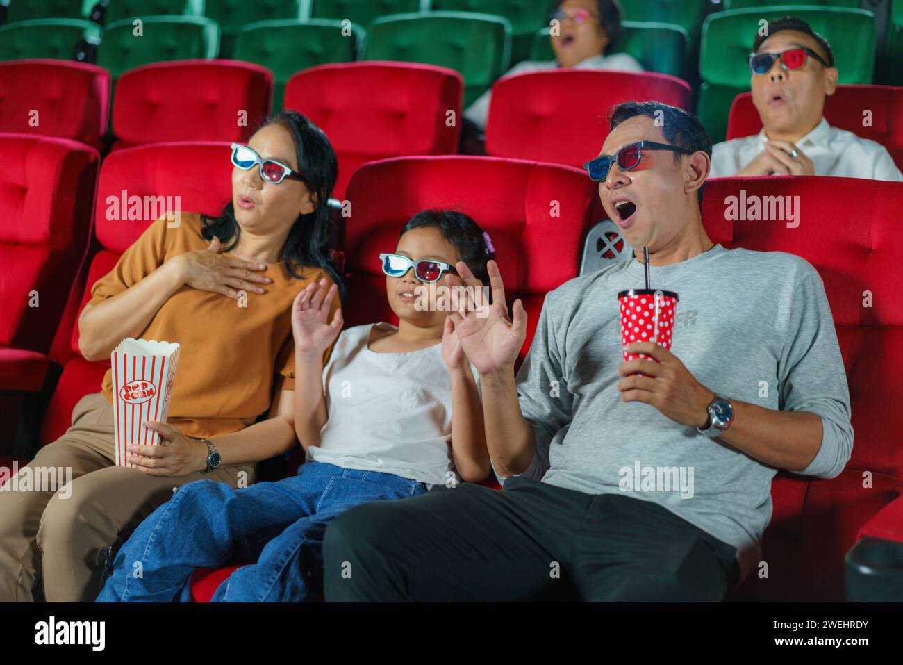 Asiatische Familie als Eltern und Kind teilen Momente der echten Überraschung, während sie einen Horrorfilm im Kino sehen. Stockfoto