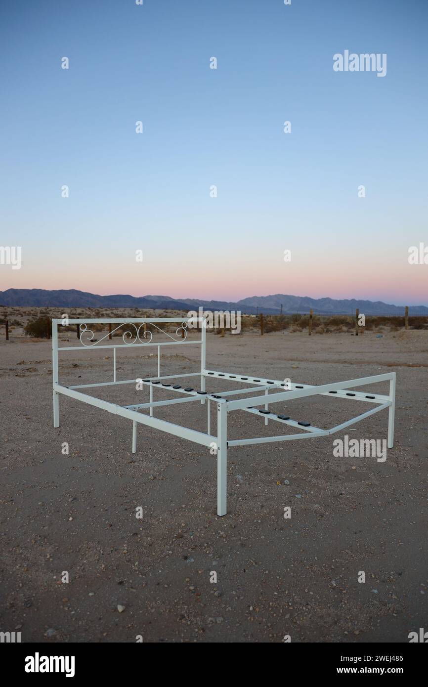 Verlassenes Bettgestell mitten in der Wüste in der Nähe von Joshua Tree, CA mit Sonnenuntergang im Hintergrund. Stockfoto