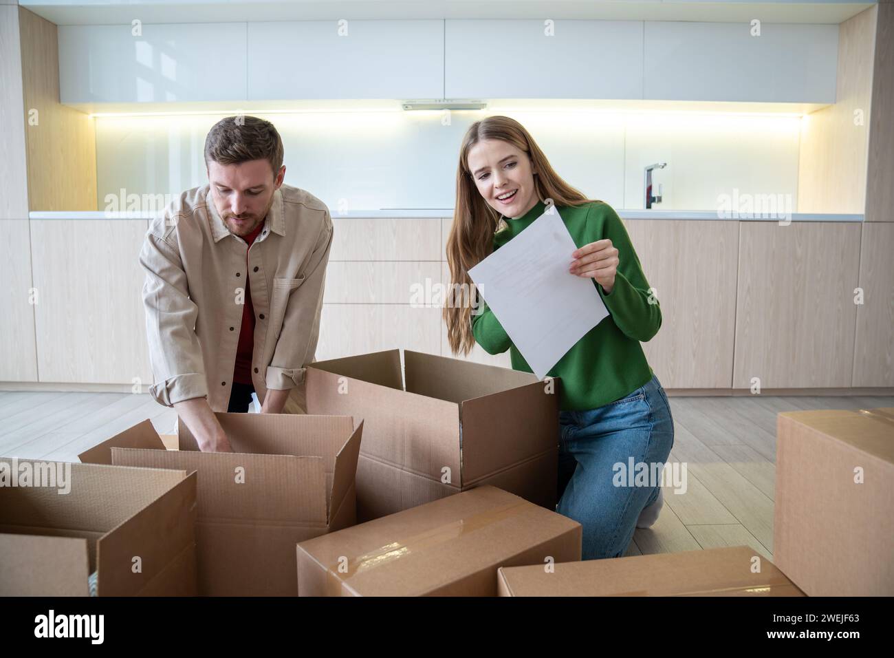 Frau und Ehemann haben die Kisten ausgepackt, nachdem sie in eine neue Wohnung gezogen sind und die Liste überprüft haben. Umzug. Stockfoto