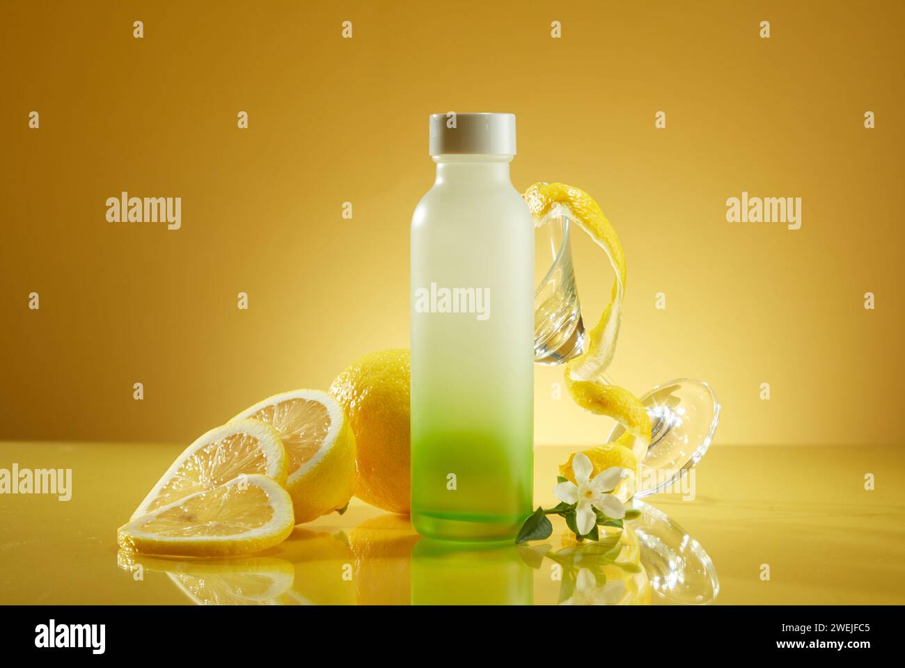 Glasflasche ohne Branding mit frischer Zitrone und Glasbecher auf gelbem Hintergrund. Verpackungen für Getränkeprodukte mit frischem Zitronengeschmack für ein r Stockfoto