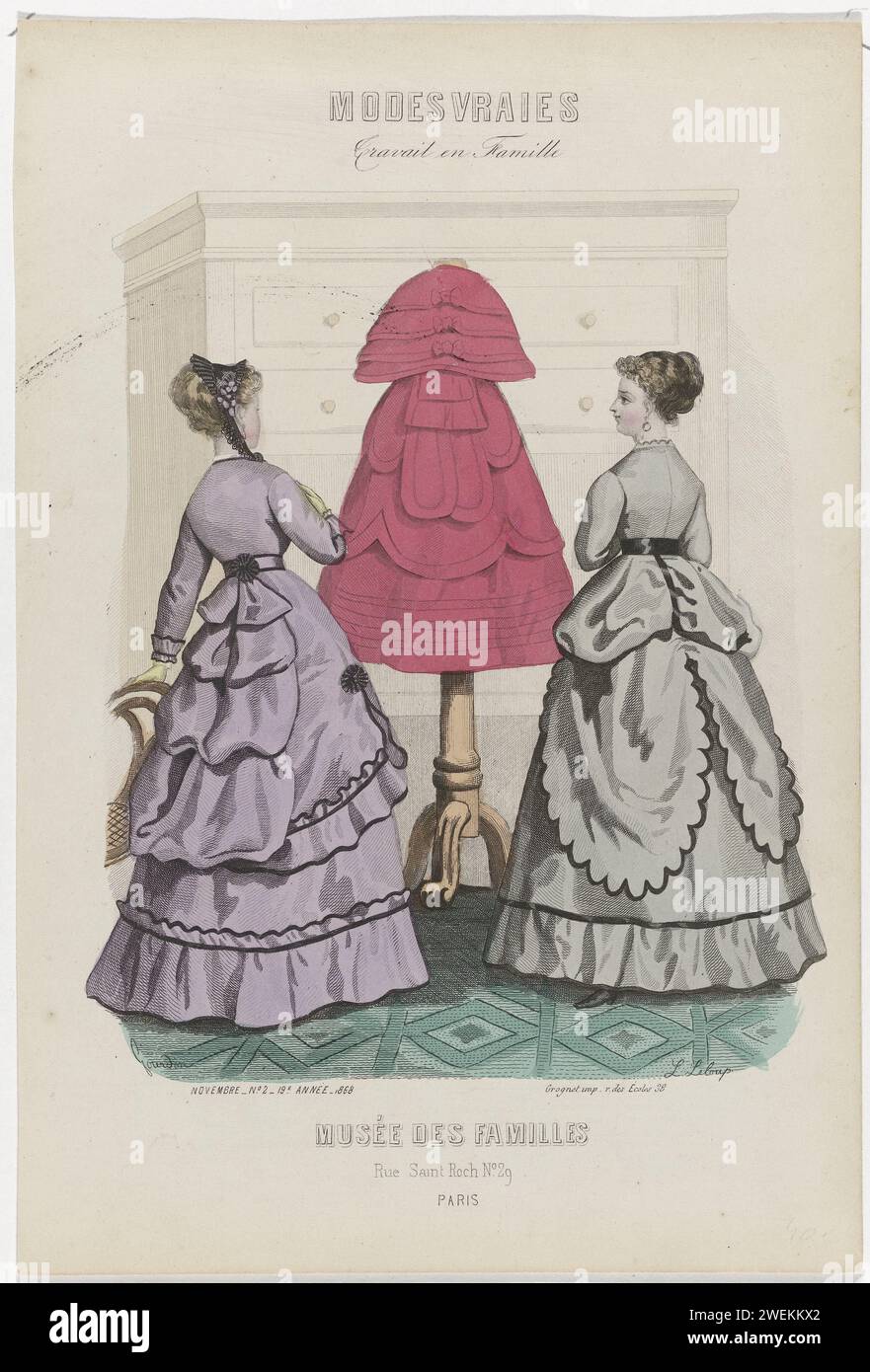 Familienmuseum, November 1868, Nr. 2, 19. Jahr, 1868 zwei Frauen, sehen Sie sich auf der Rückseite ein Modell an einer Schaufensterpuppe an. Eine große Kommode im Hintergrund. Links: Hellviolettes Kleid mit mittlerer Draperation. Rechts: Hellgraues Kleid mit gewelltem Saum und schwarzer Paspelierung. Druck aus dem Modemagazin Musée des Familles (1833-1874). Papiergravur von Modetafeln. Kleid, Kleid (+ Damenkleidung). Kopfbedeckung (+ Damenkleidung). Schaufensterfiguren (+ Damenbekleidung). Schrank. Ohrringe (+ Damenkleidung) Stockfoto