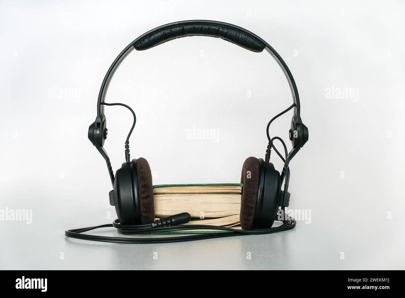 Ein Taschenbuch mit Kopfhörern und einem Mini-Klinkenstecker, der zwischen den Seiten auf hellem Hintergrund eingesteckt wird. Der Begriff des Hörbuchs Stockfoto