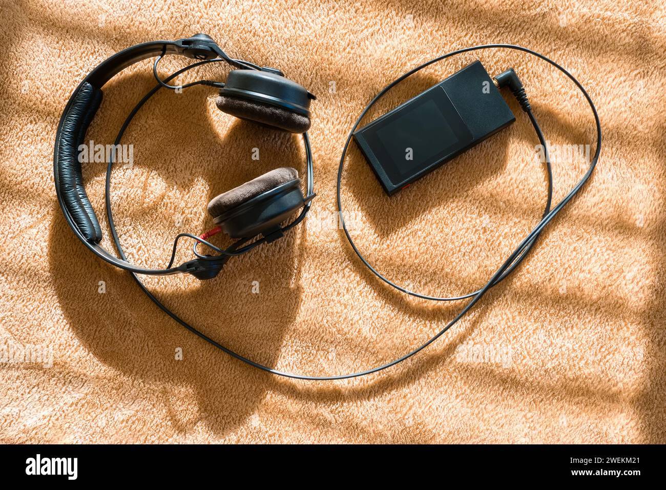 Blick von oben auf Kopfhörer und hochauflösenden Audio-Player auf einem weichen Karo in Sonnenstrahlen durch Jalousien. Hintergrund Stockfoto