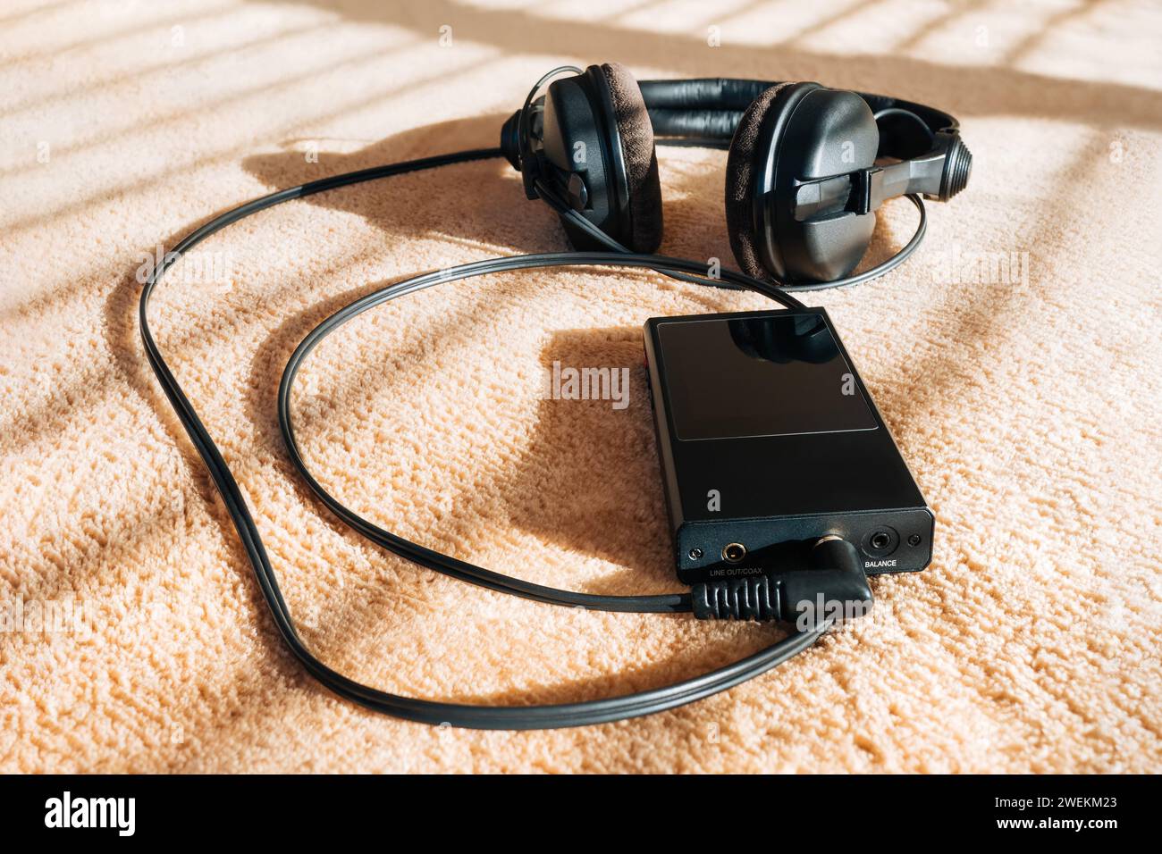Kopfhörer und hochauflösender Audio-Player auf weichem Karo in Sonnenstrahlen durch Jalousien. Hintergrund Stockfoto