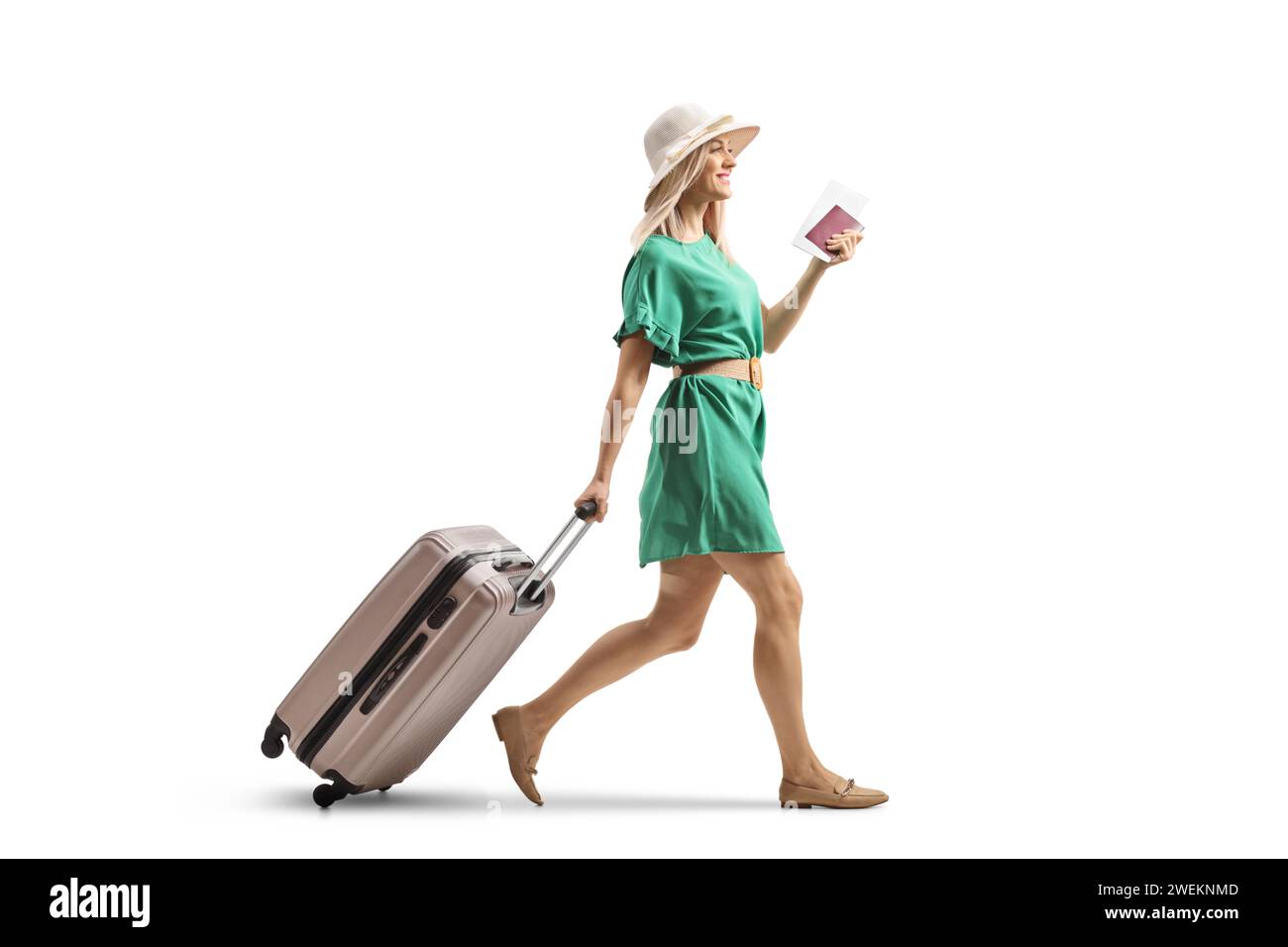 Junge Frau in einem grünen Kleid, die einen Koffer zieht und einen Pass auf weißem Hintergrund hält Stockfoto
