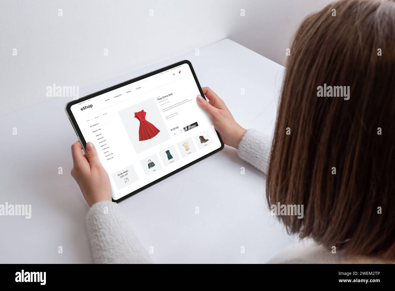 Die Frau hält ein Tablet mit einer E-Commerce-Webseite, auf der Suche nach einem roten Kleid. Moderne Einkaufsmöglichkeiten auf Knopfdruck, die Technologie und Mode in einem Kontingent verbinden Stockfoto