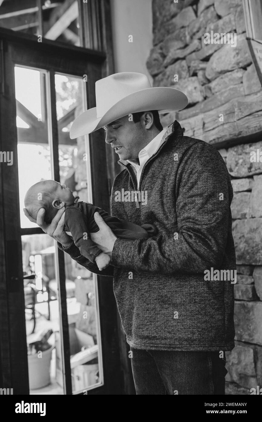 Dad im Cowboyhut hält den neugeborenen Sohn und lächelt fröhlich Stockfoto