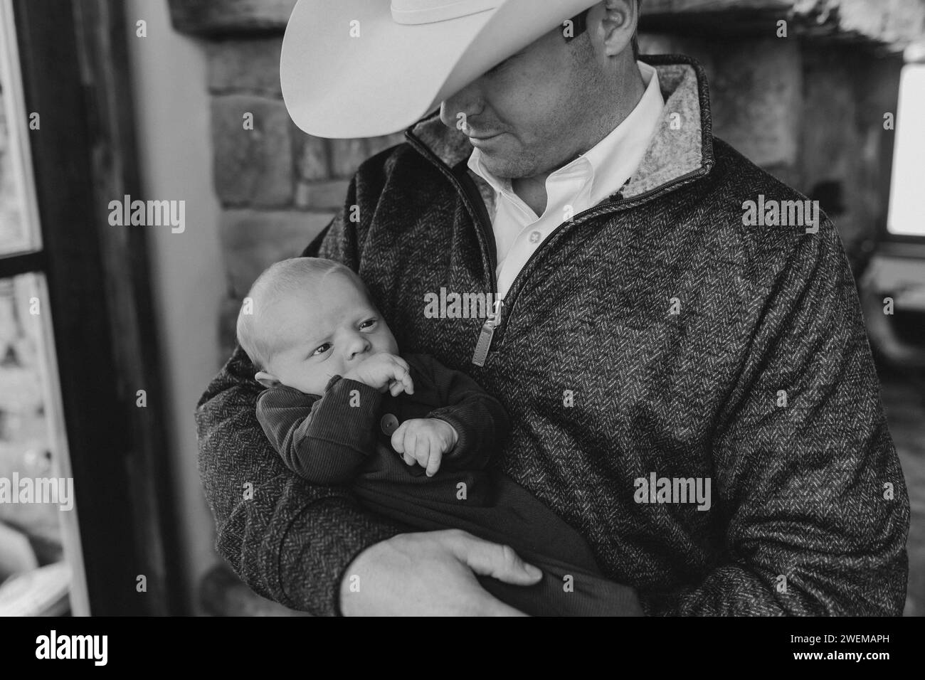 Dad im Cowboyhut hält den neugeborenen Sohn und lächelt fröhlich Stockfoto