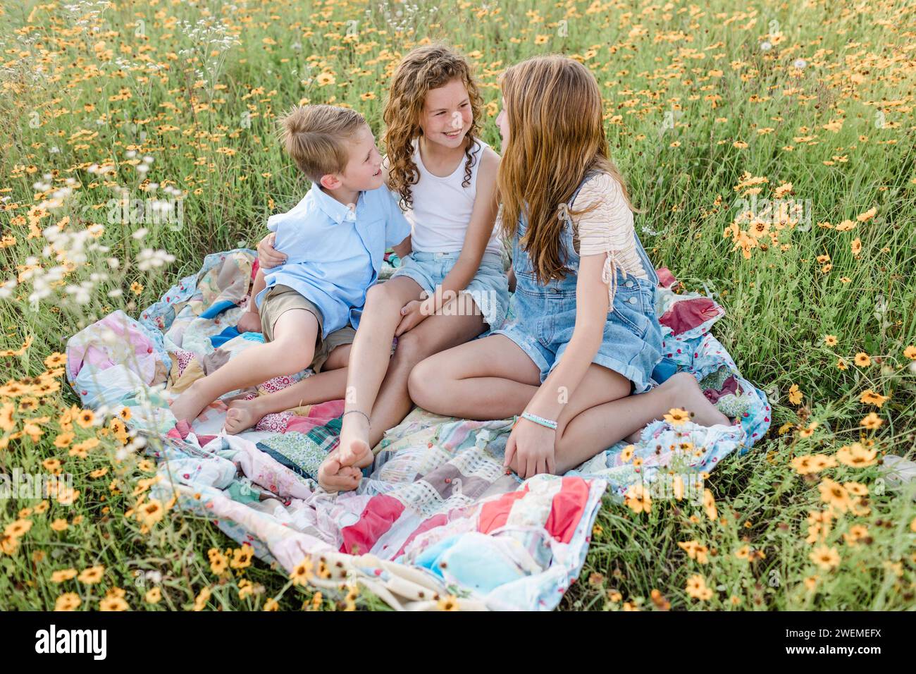 Geschwister sitzen an einem Frühlingstag auf einem Quilt in einem Blumenfeld Stockfoto