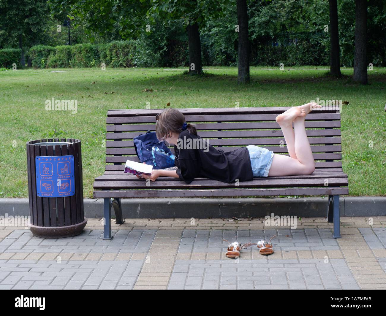 Ein Mädchen liegt mit einem Buch auf einer Parkbank. Stockfoto