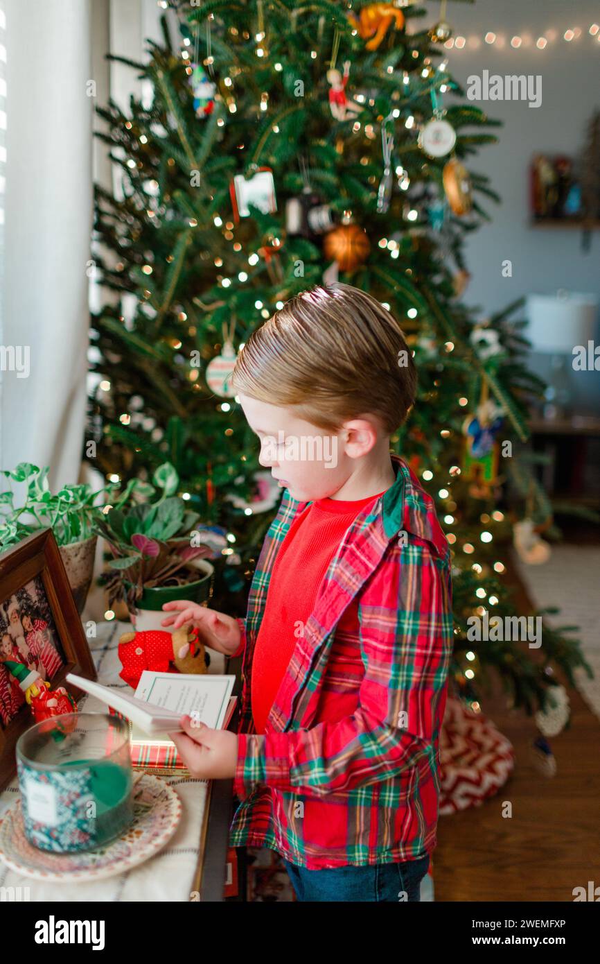 Junge, der vor dem weihnachtsbaum steht und ein Buch liest Stockfoto
