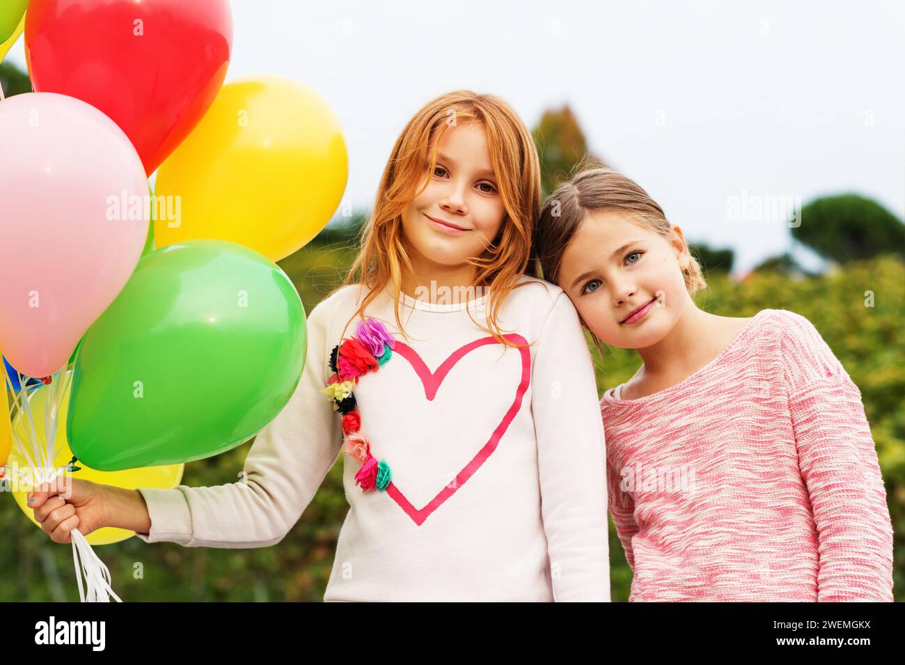 Außenporträt von 2 süßen kleinen Mädchen mit bunten Ballons Stockfoto