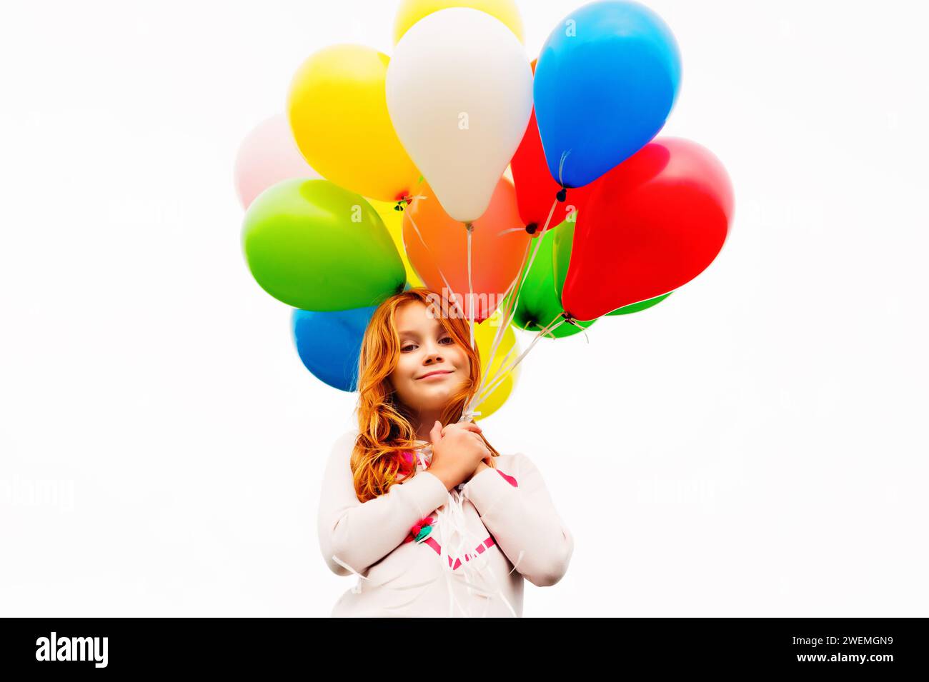 Glückliches 8-9-jähriges Mädchen mit rotem Haar, das bunte Heliumballons hält Stockfoto