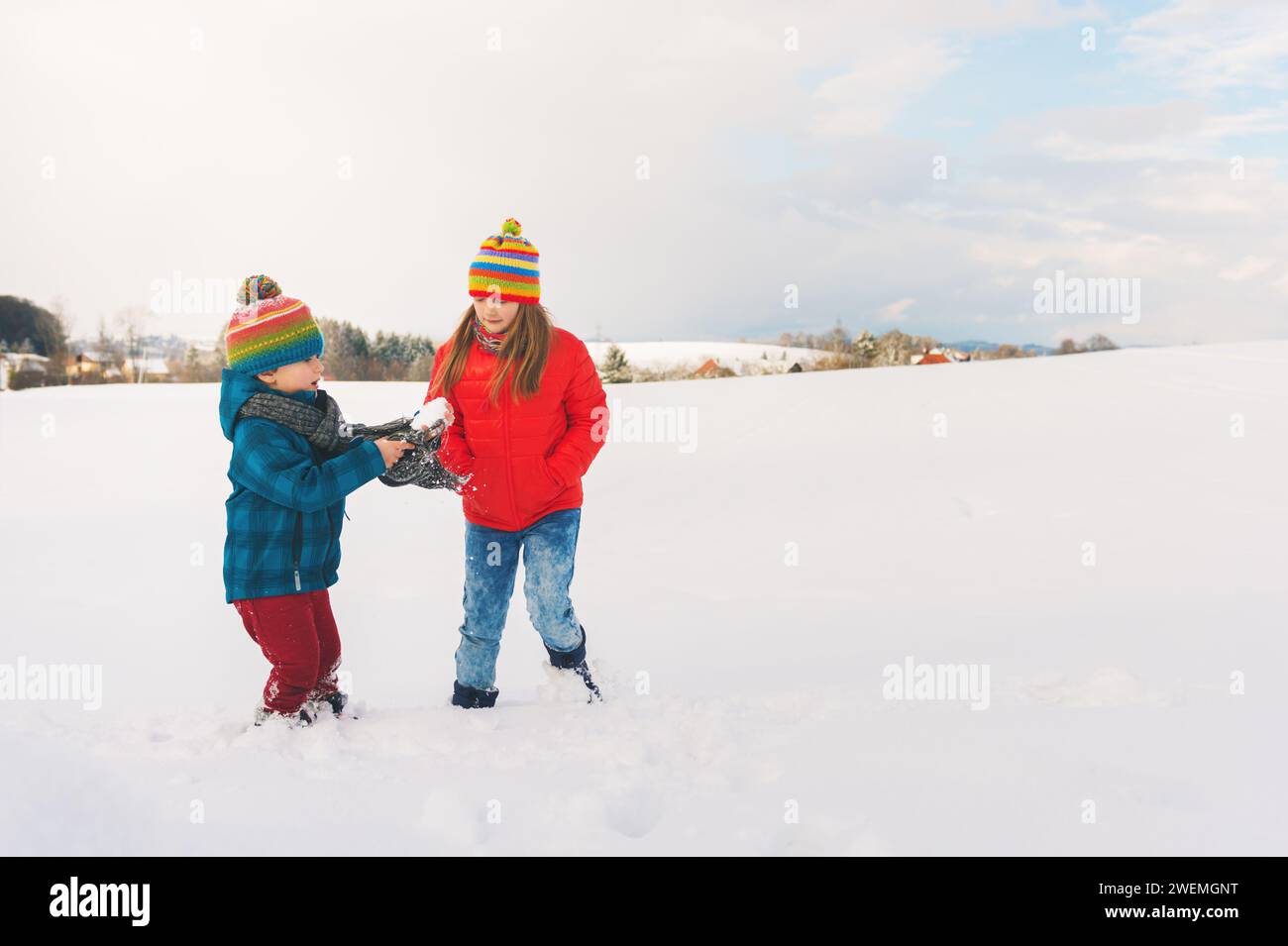 Niedliche kleine Kinder spielen zusammen auf dem Schneefeld, tragen warme Jacken und Hüte Stockfoto