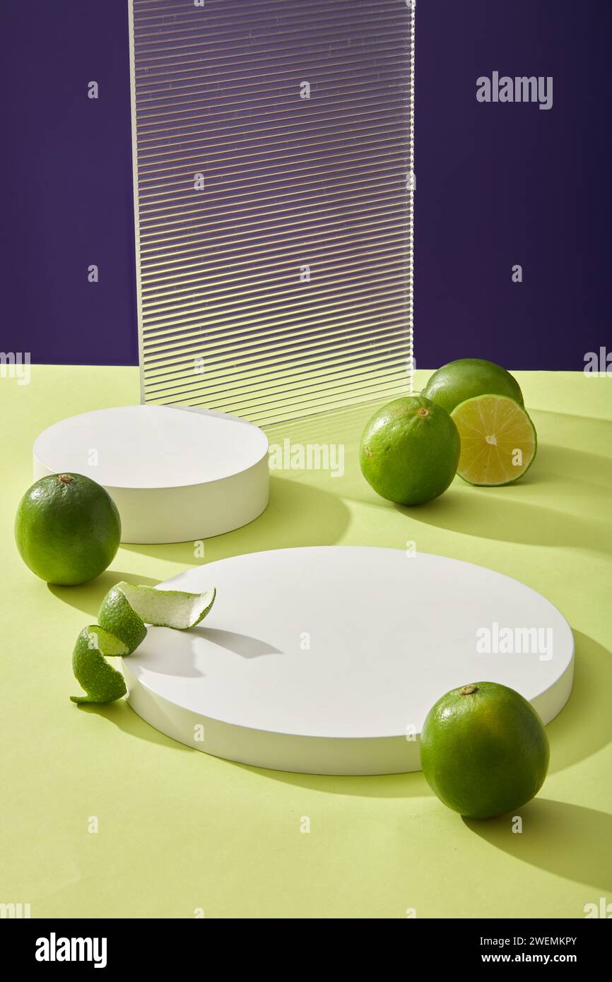 Rundes leeres Podium, Acrylplatte und frische Limettencitrus (Citrus aurantifolia) auf farbigem Hintergrund. Plattform für Displaykosmetik von Kalkextrakt. Mini Stockfoto