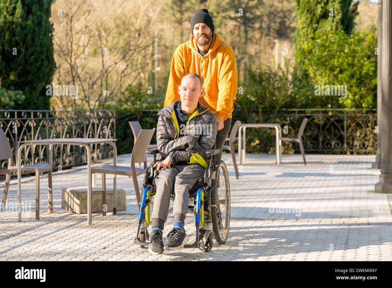 Entspannter behinderter Mann mit Rollstuhl und Freunde, die in einem Stadtpark spazieren Stockfoto