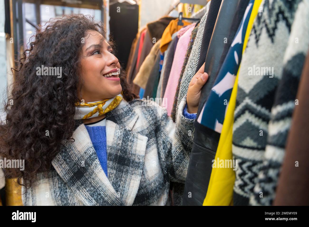 Porträt einer lächelnden Frau, die Kleidung in einem alten Second-Hand-Laden aussieht Stockfoto