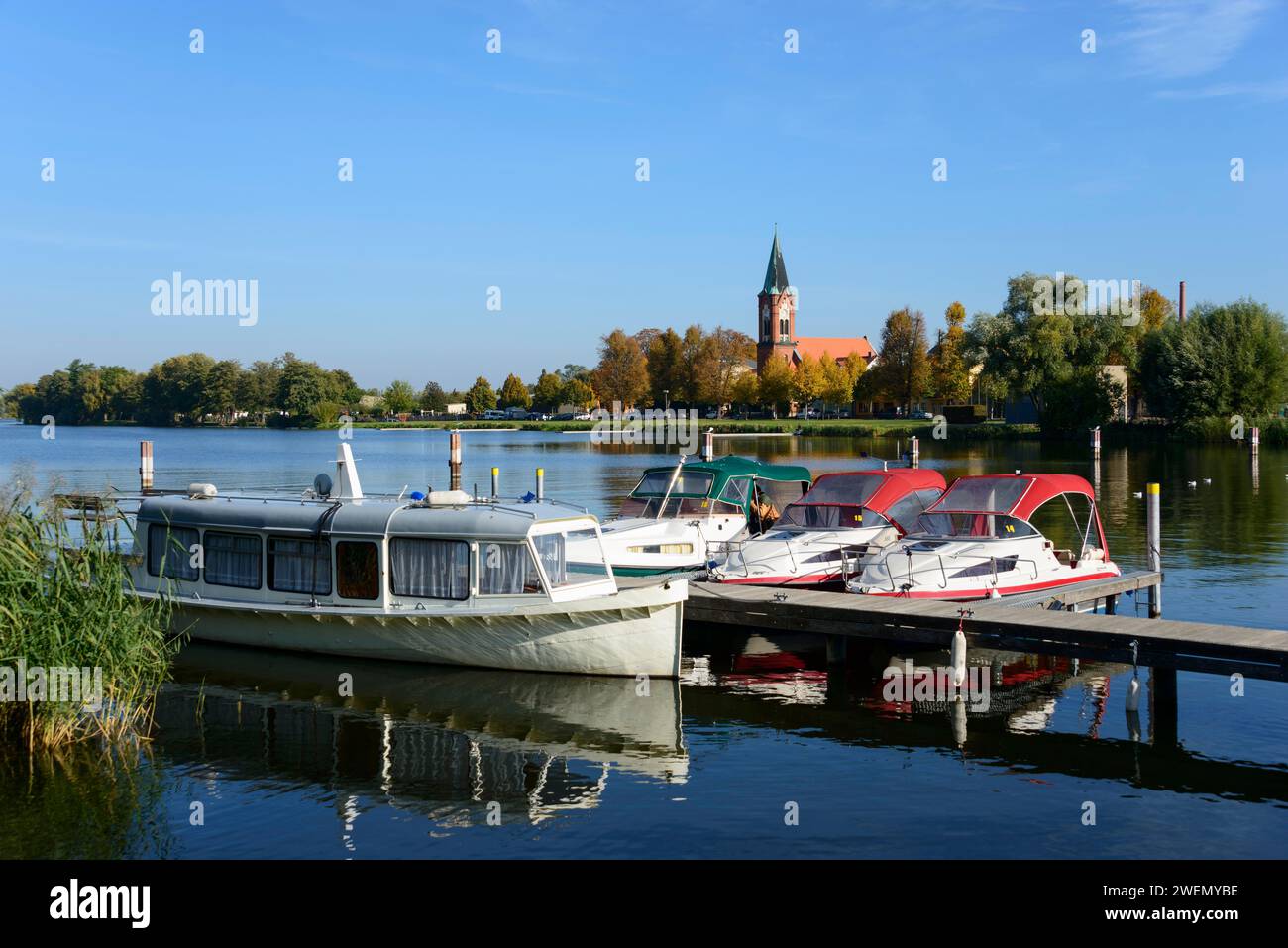 Boote, die auf einem ruhigen See vor einer Kirche liegen, umgeben von Bäumen unter klarem blauem Himmel, Schiffe, Hafen, Kirche Maria Meeresstern, Werder, Insel Stockfoto