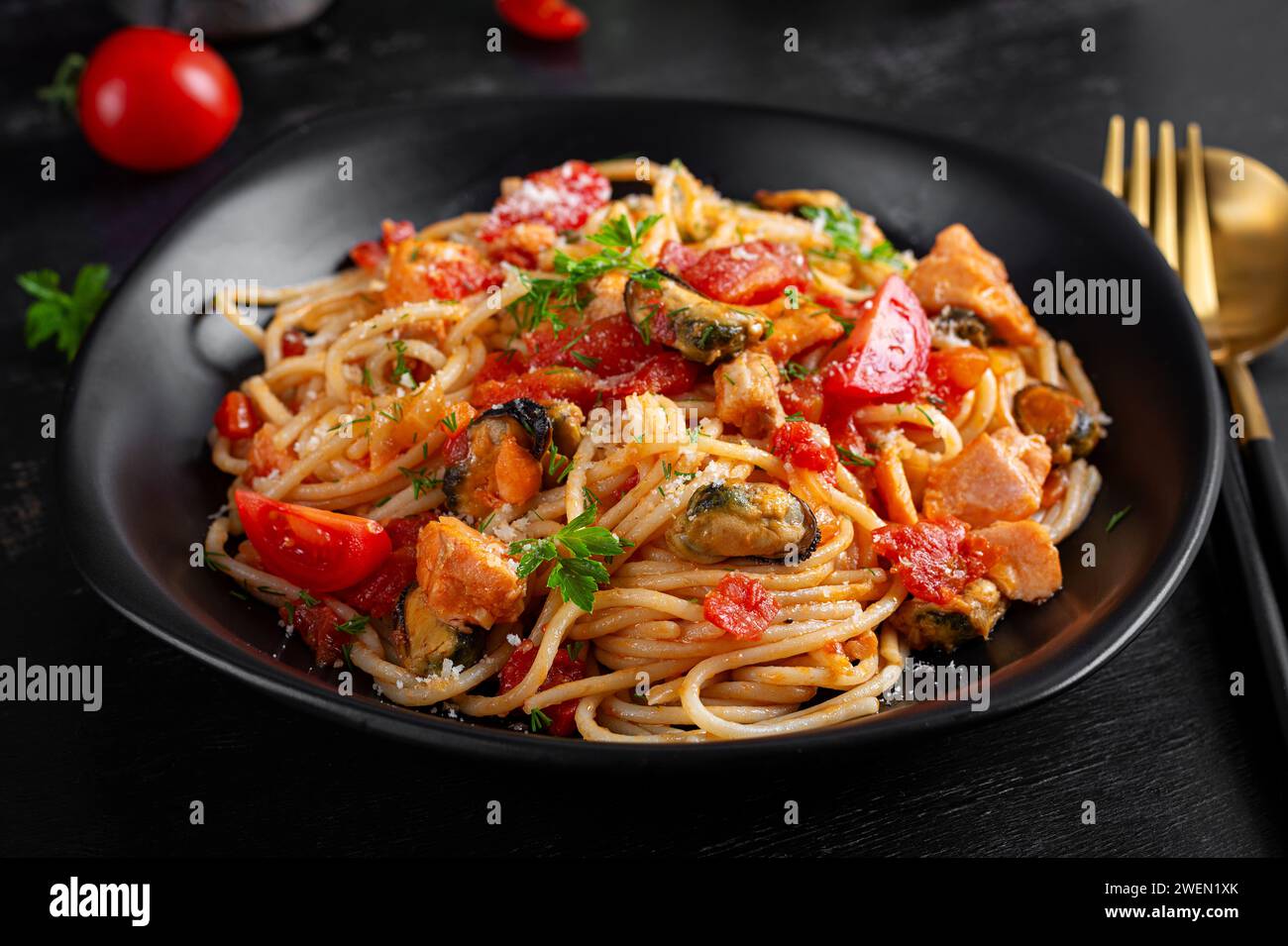 Klassische italienische Pasta Spaghetti Marinara mit Muscheln und Lachs auf dunklem Tisch. Spaghetti-Pasta mit Marinara-Sauce. Stockfoto