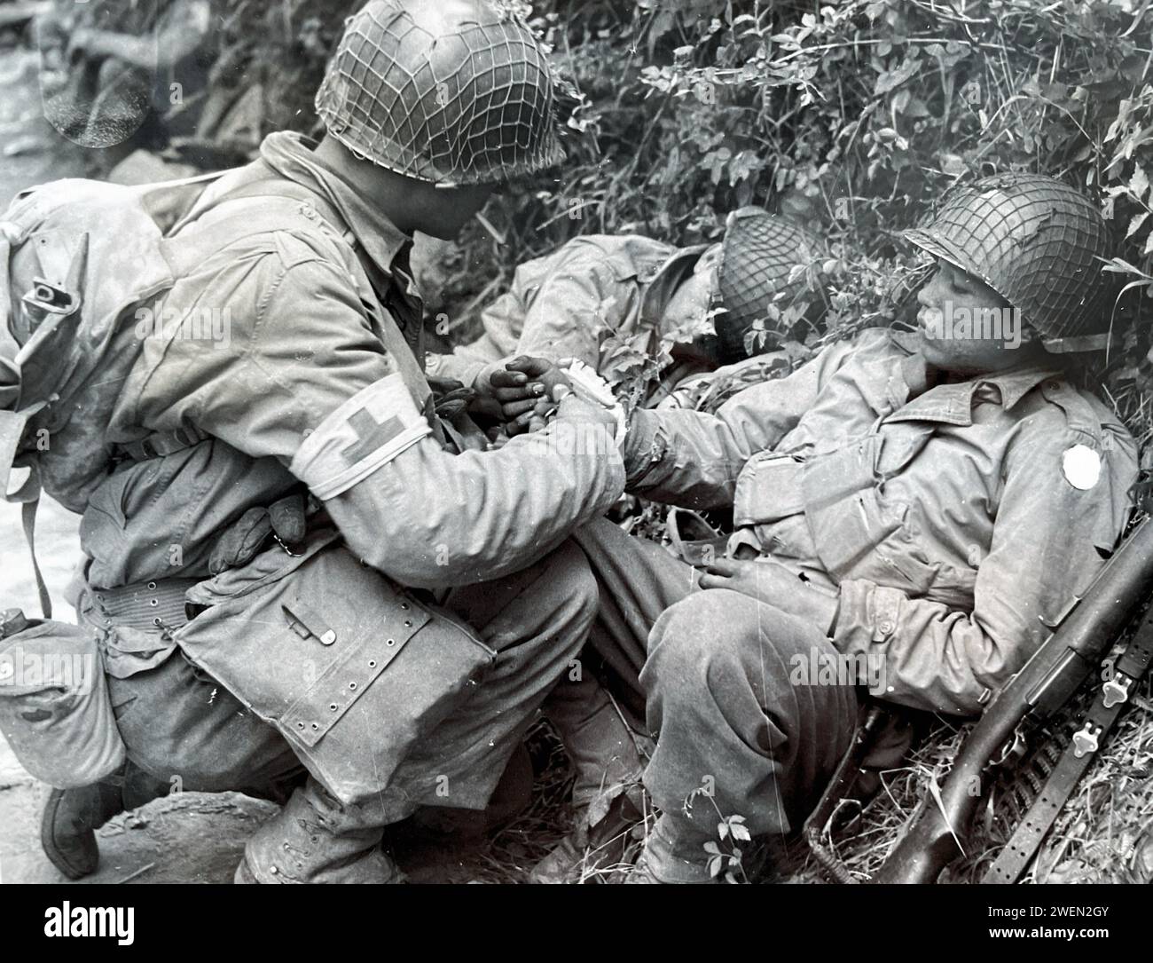 OPERATION OPERLORD Juni 1944. Ein US-Sanitäter kümmert sich um einen verwundeten Soldaten. Beachten Sie, dass der Zensor das Abzeichen der Einheit des Verwundeten verdeckt hat. Stockfoto