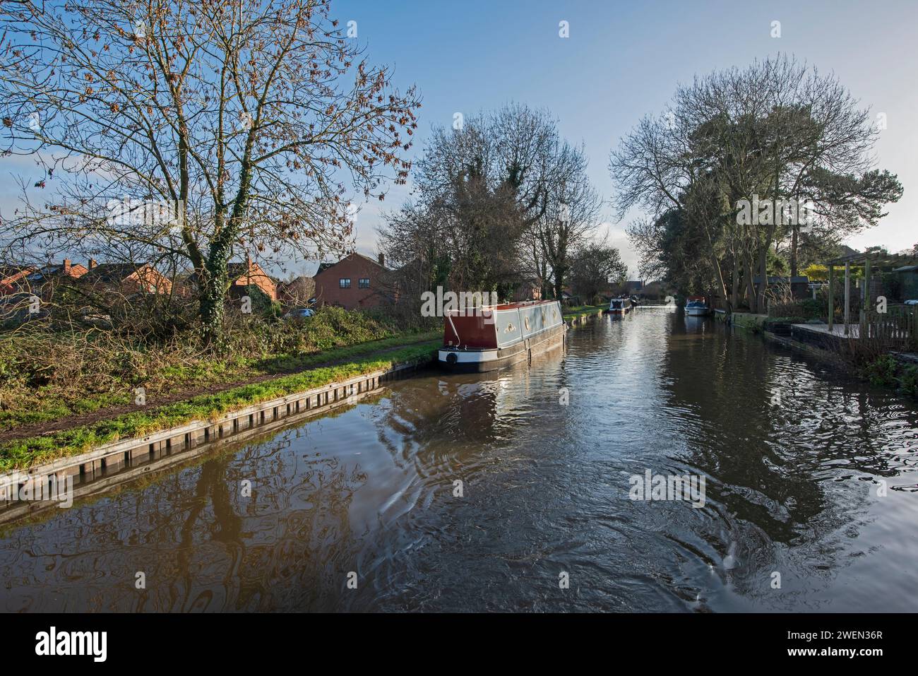 Blick aus einem Schmalboot, das durch englische städtische Dörfer auf dem britischen Wasserstraßenkal mit festgemachtem Boot fährt Stockfoto